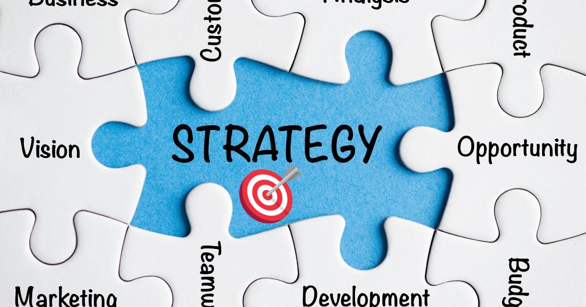 Strategy written on blue background on non-completed white puzzle pieces with words like marketing, vision, opportunity