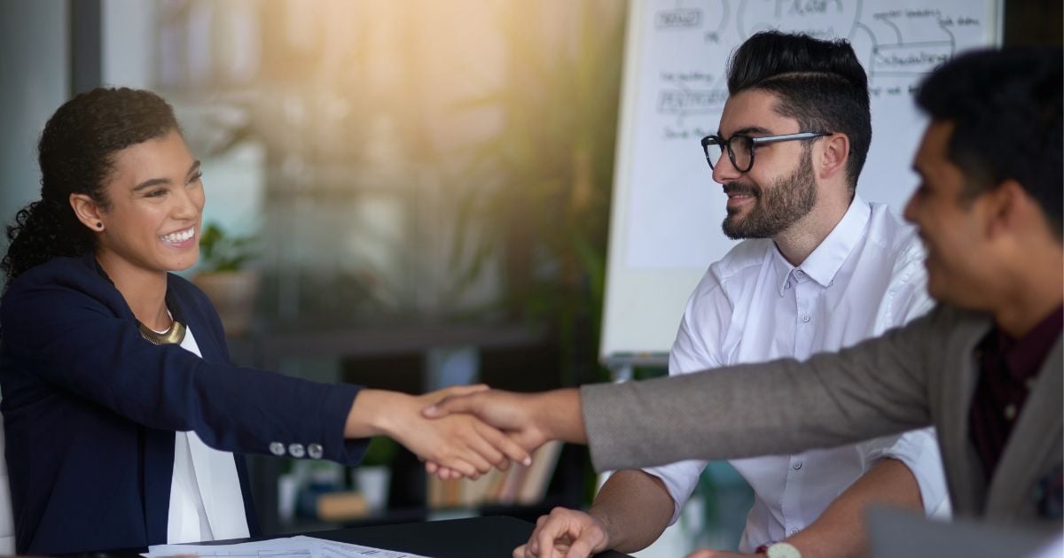 People sitting at a conference table, with two people shaking hands and smiling