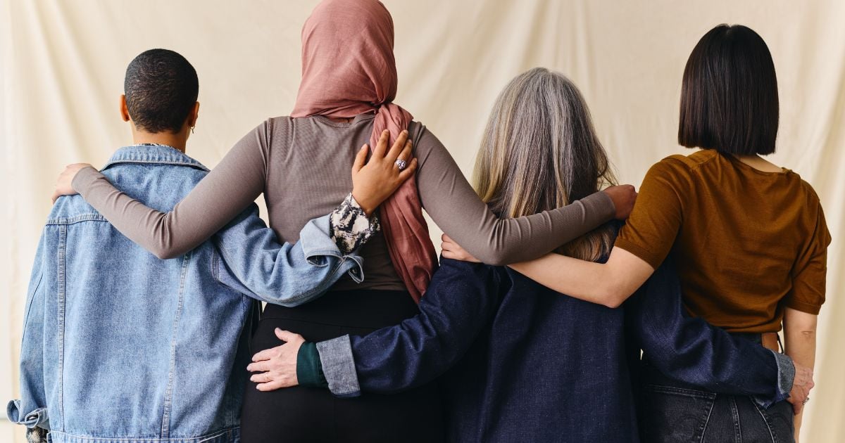 Rear view of four women with arms around each other for support